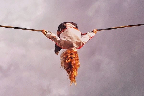 Kvinde hænger med hovedet nedad og holder fast i reb på en baggrund af skyer